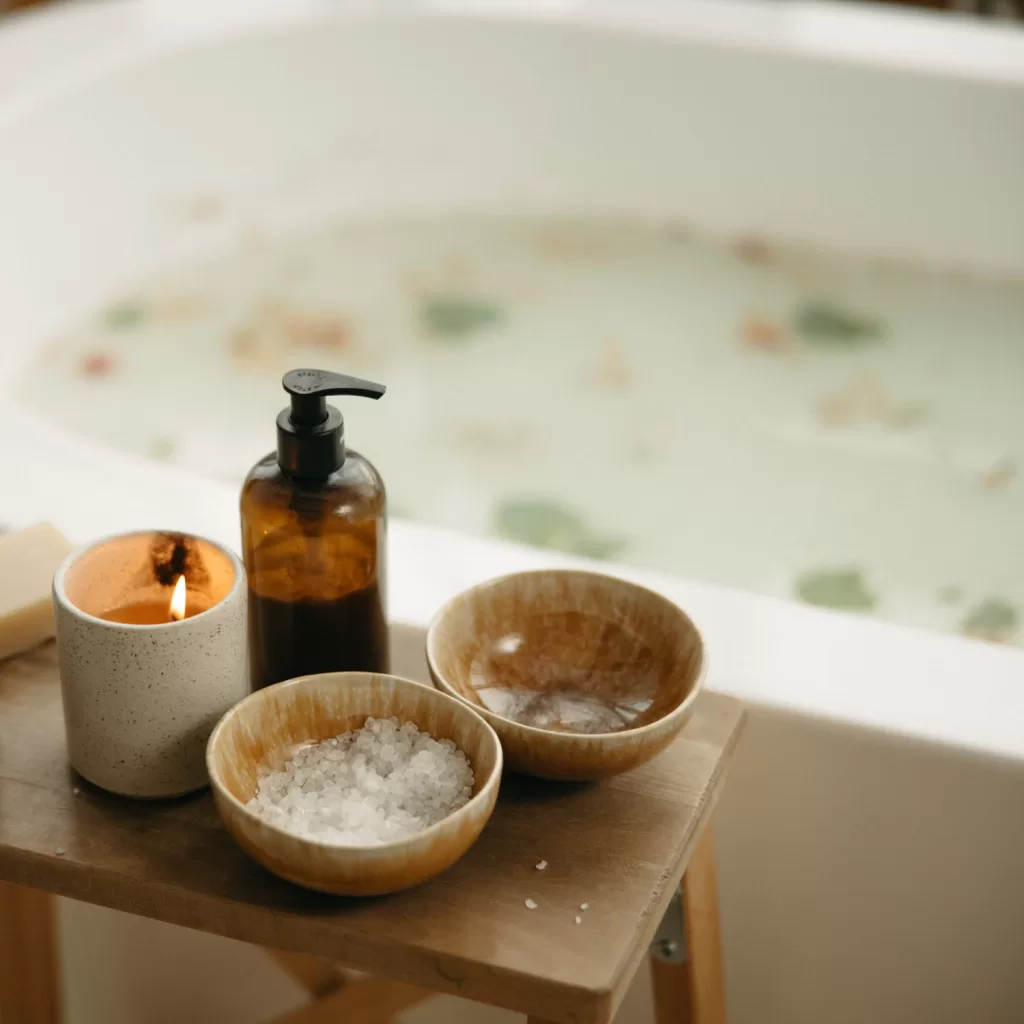 Cozy winter bath setup with a candle, pump bottle, and bowls of salts, perfect for relaxation and winter wellness.