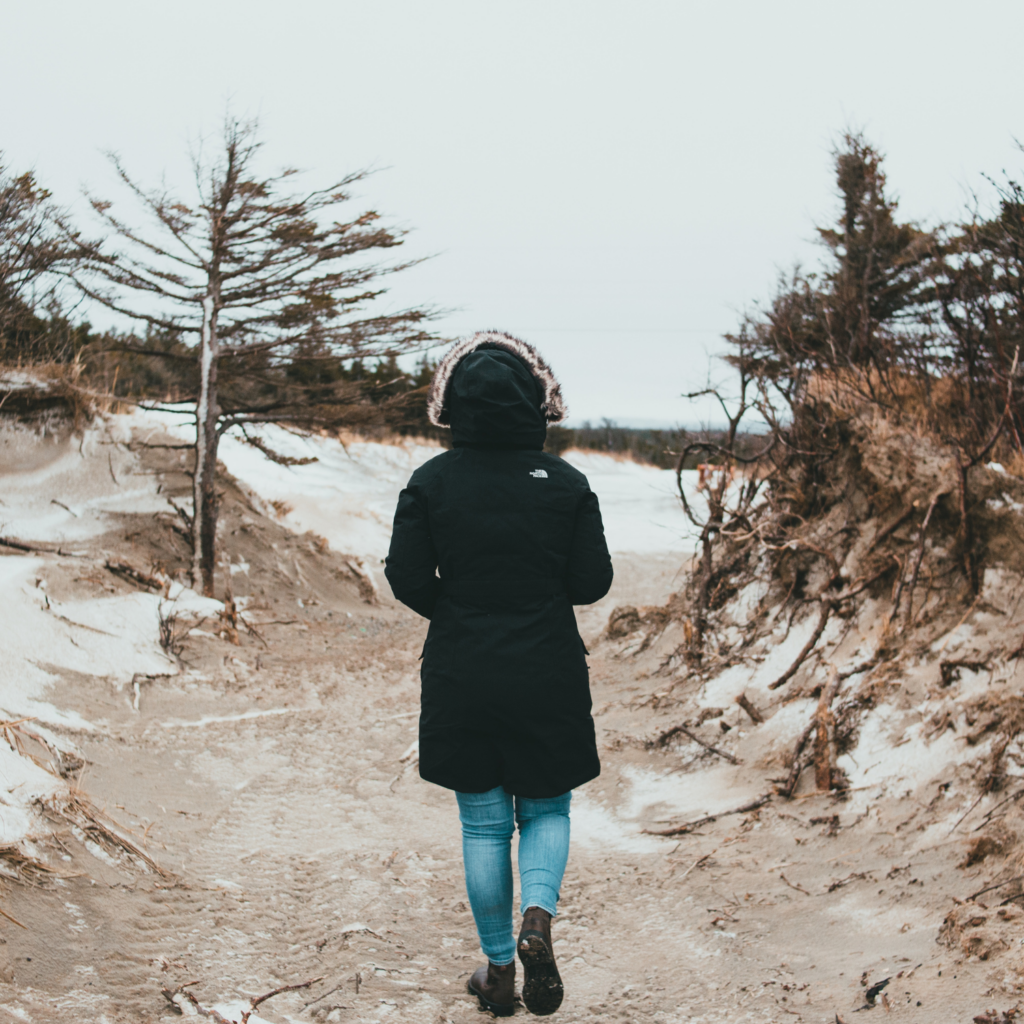 Person walking in winter nature near a beach with sand, bluffs, and trees, embracing the outdoors during winter.