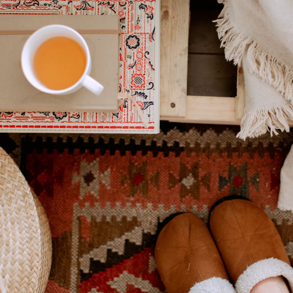 Comforting cup of tea on a table with a cozy blanket and slippered feet, ideal for winter self-care and relaxation.