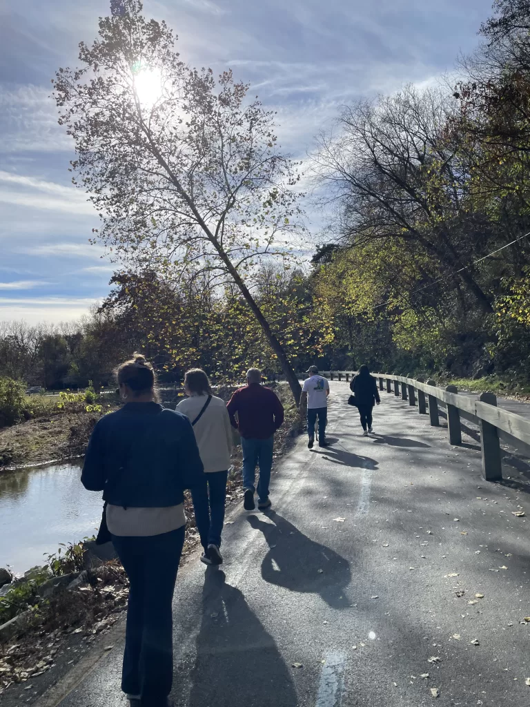 Family walking on a sunny path next to a river in Luray, Virginia, surrounded by nature and blue skies.