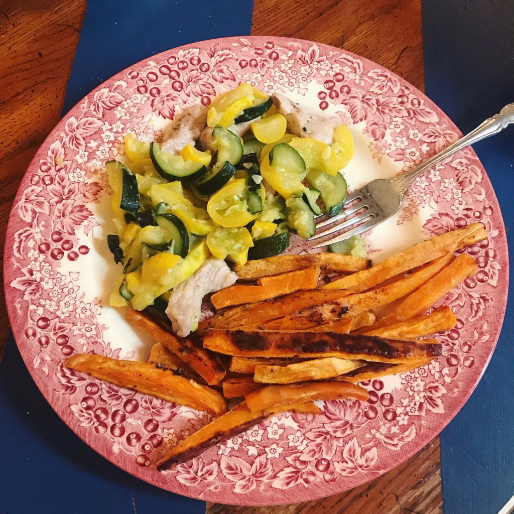 Plate of AIP-friendly dinner featuring roasted sweet potato fries, sautéed zucchini and summer squash, and grilled chicken breast.