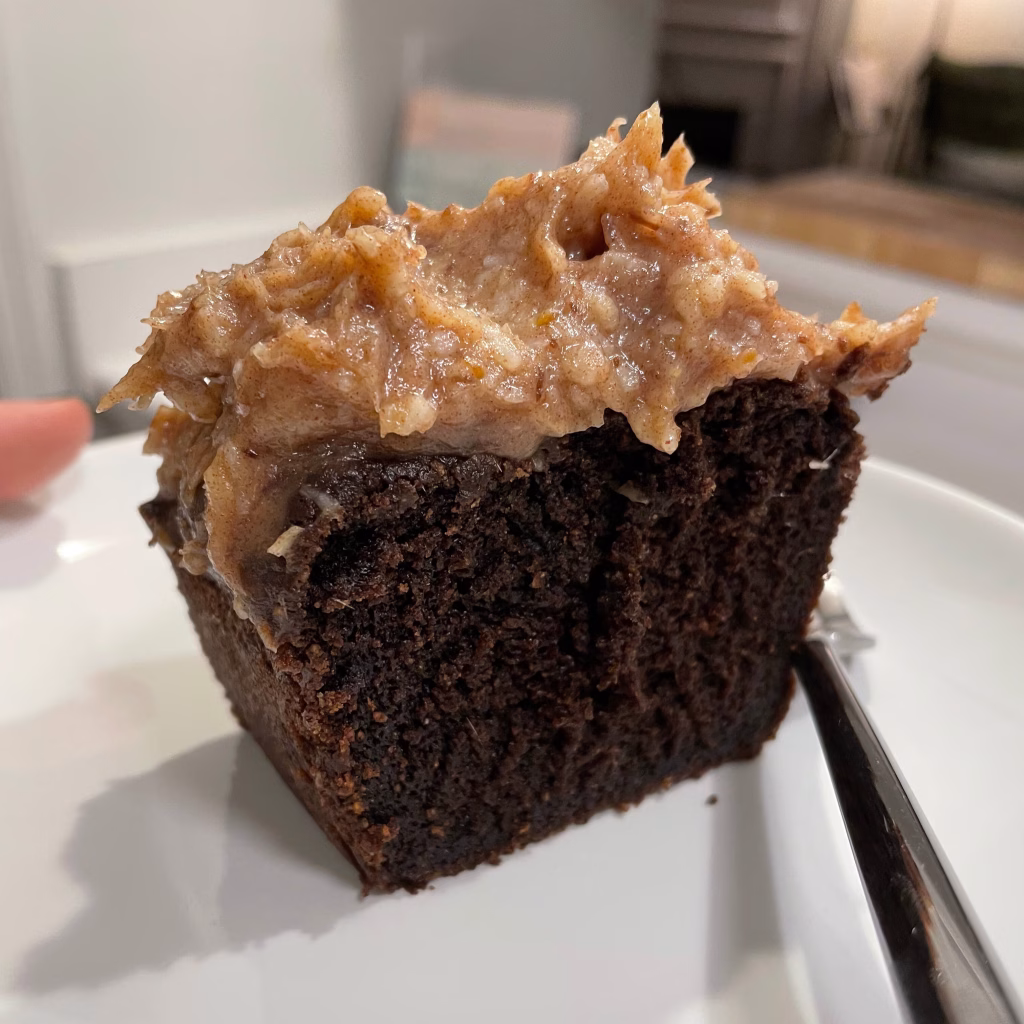 A slice of AIP-friendly carob cake topped with creamy coconut date caramel frosting on a white plate.